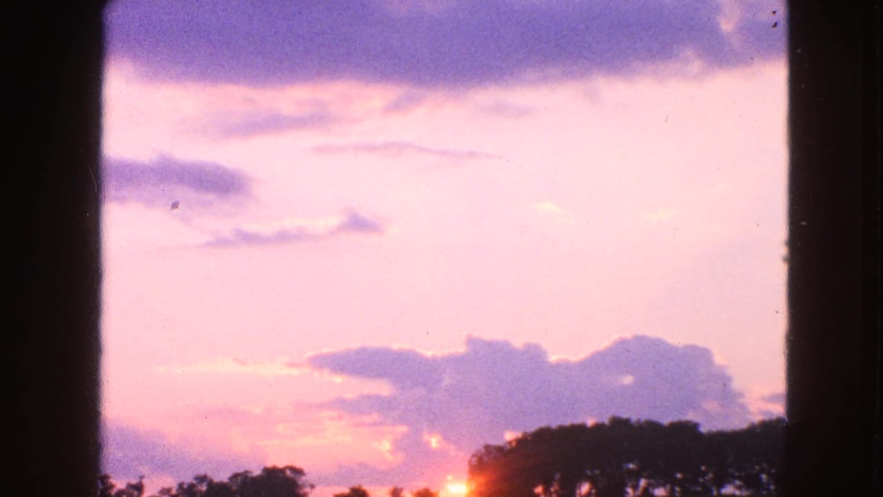 1963 Walworth, Wisconsin 8mm frame showing a soft sunrise glow behind a rural treeline under pink and purple clouds.
