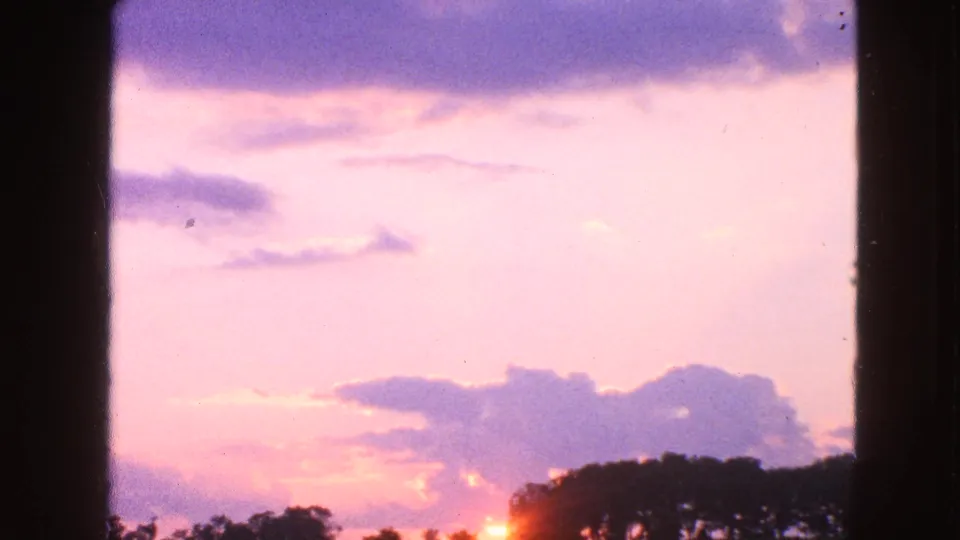 1963 Walworth, Wisconsin 8mm frame showing a soft sunrise glow behind a rural treeline under pink and purple clouds.