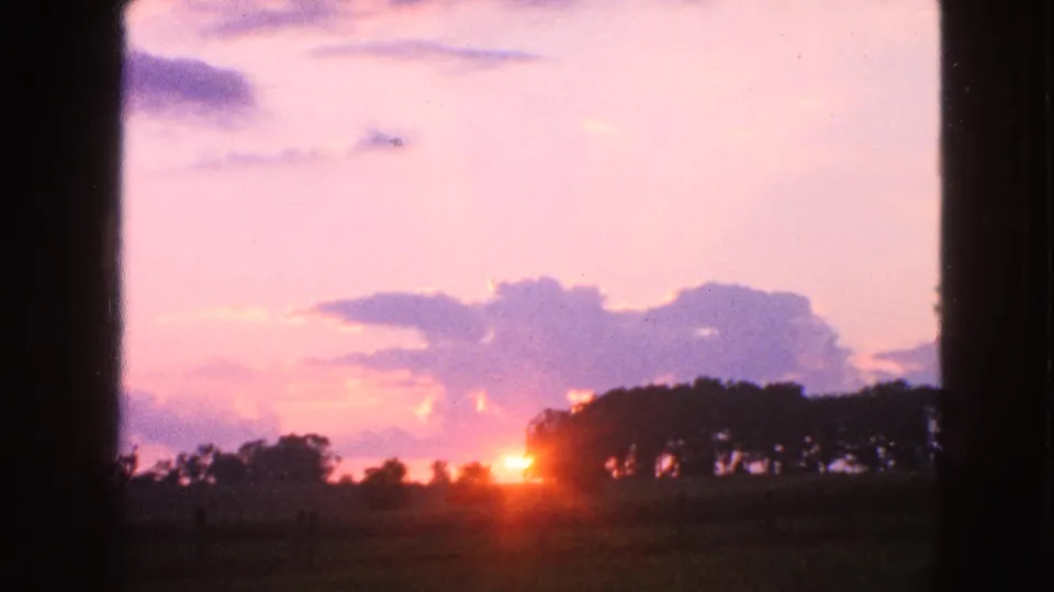 Final 1963 Walworth sunrise frame with orange light low on the horizon, silhouetted trees, soft clouds, and visible 8mm film texture.