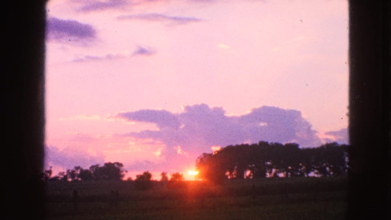 1963 Walworth, Wisconsin 8mm frame showing a low sun near a tree line, pink clouds, open field, and dark framing at the sides.