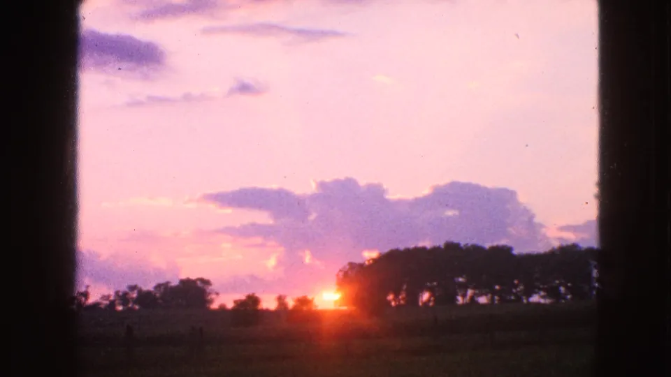 1963 Walworth, Wisconsin 8mm frame showing a low sun near a tree line, pink clouds, open field, and dark framing at the sides.