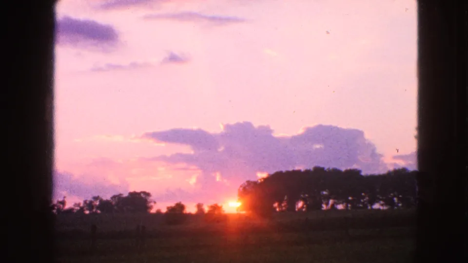1963 Walworth, Wisconsin home-movie frame with the sun at the horizon, cloud bands, distant trees, and dark side framing.