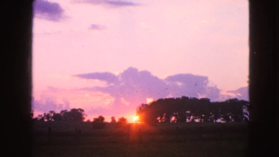 1963 Walworth, Wisconsin frame of a rural sunset with pink clouds, dark trees, open field, and strong exposure bloom around the sun.