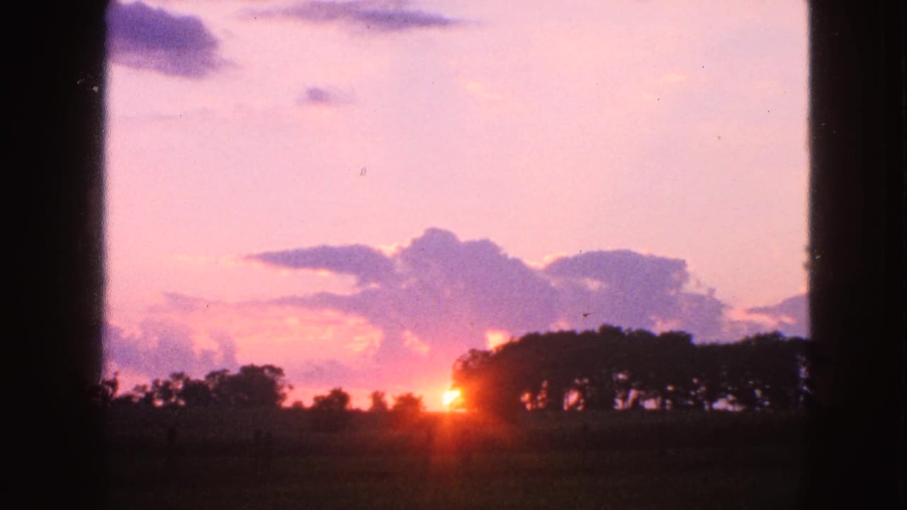 1963 Walworth, Wisconsin 8mm frame showing the sun near the horizon behind silhouetted trees and a dark field.