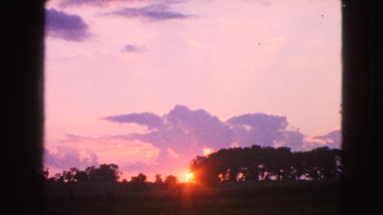 1963 Walworth, Wisconsin sunset view with a bright sun flare near the tree line and dark structural edges framing the scene.