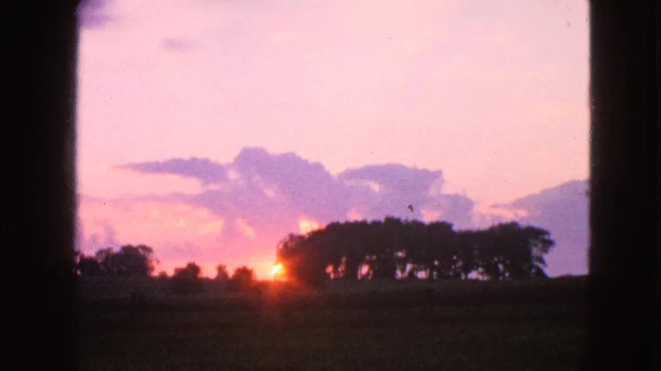 1963 Walworth, Wisconsin home-movie frame of a sunset over fields, partly bordered by dark window or gate edges.