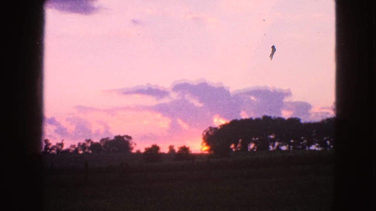 1963 Walworth, Wisconsin 8mm frame showing a pink-purple sunset behind silhouetted trees and farmland, bordered by dark interior framing.