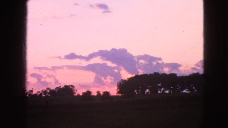 1963 Walworth, Wisconsin 8mm still of a rural sunset with silhouetted trees, open field, and aged film color shifts.