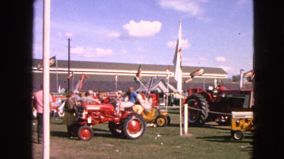 The camera holds on red and yellow tractor displays with spectators, flags, and show structures in the background.