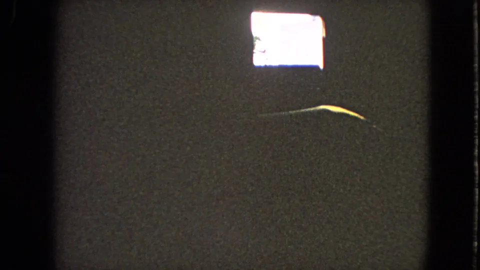 Dark 8mm reel-end frame with a bright rectangular flare, visible grain, and a thin curved streak across the lower center.