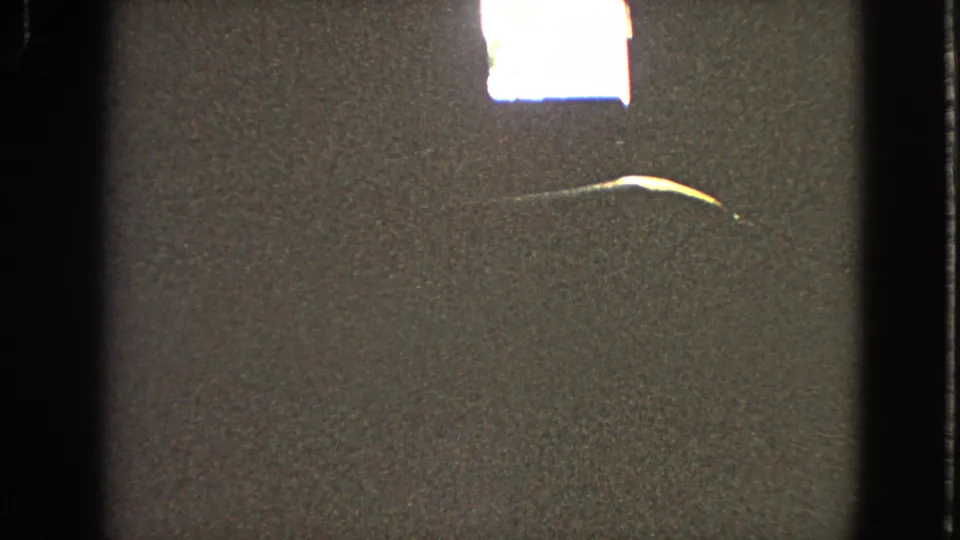 Final dark 8mm frame showing a bright flare near the top, grainy texture, a curved streak, and film-gate edges.