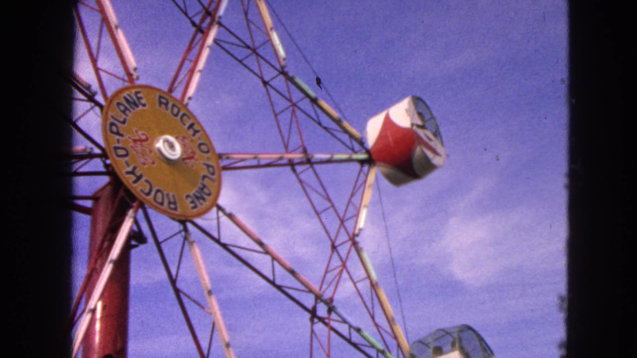 1963 Walworth, Wisconsin frame of the Rock-O-Plane ride with its yellow hub sign and red and white cab rotating overhead.