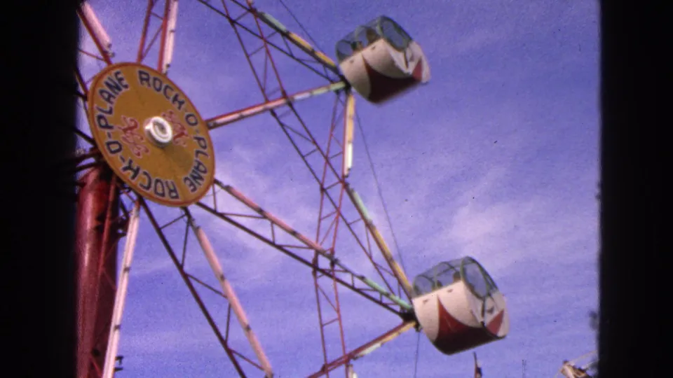 Home-movie frame from the 1963 Walworth clip showing the Rock-O-Plane structure with two enclosed cabs visible against the sky.