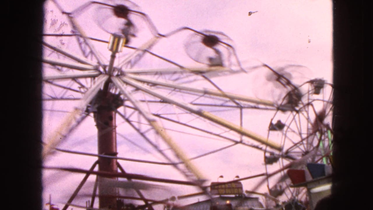 Fast-spinning Ferris wheel with blurred passenger cars against a pink sky.