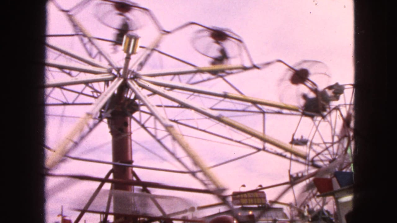 1963 Walworth, Wisconsin fairground frame with the Ferris wheel rotating fast, open cars swinging outward and small riders visible in motion blur.