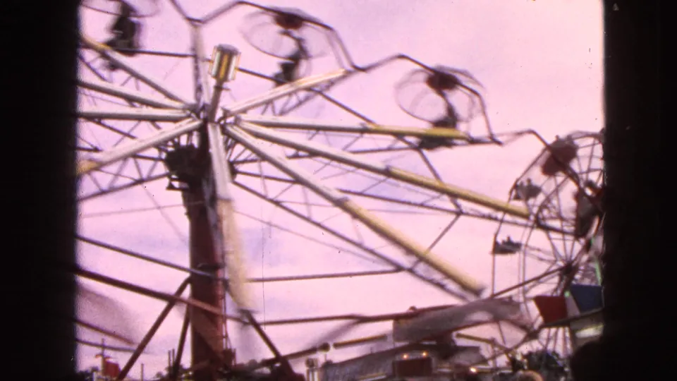 1963 Walworth, Wisconsin 8mm view of a Ferris wheel from below, with the central hub, support beams, and fast-moving cars softened by motion.