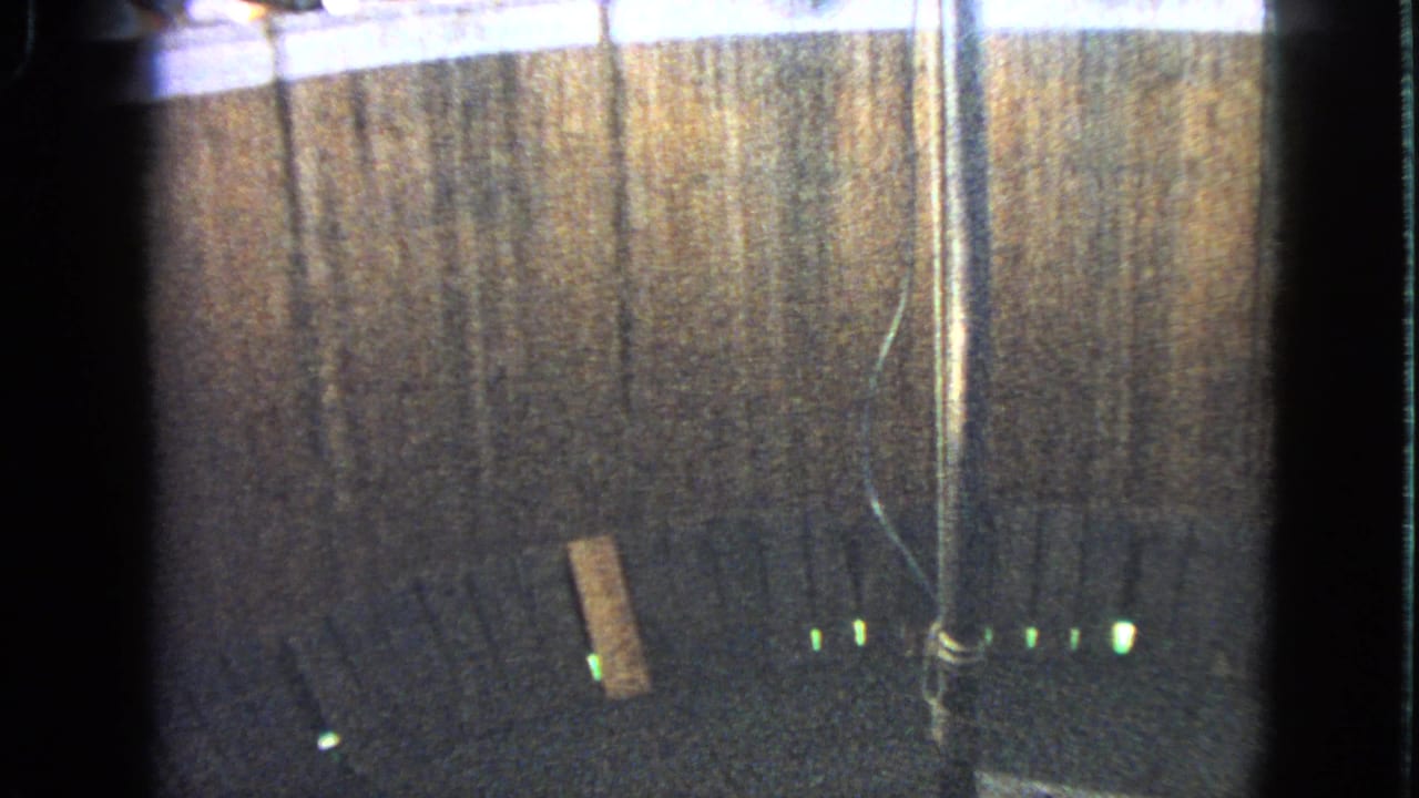 1963 Walworth, Wisconsin 8mm frame showing the racecourse surface, barrier, pole, loose plank, and green track-edge lights without a clear rider.