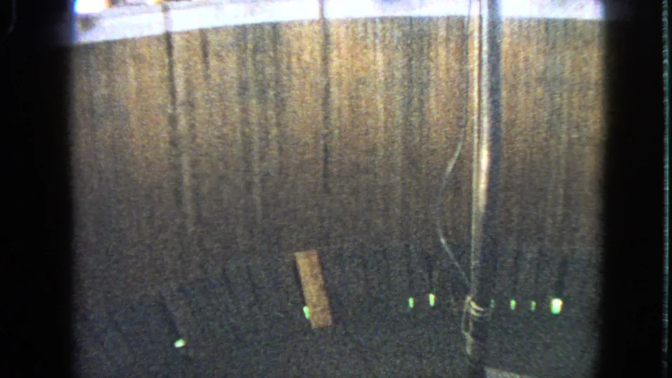 1963 Walworth home-movie frame showing the dim wooden interior of a circular motorcycle stunt structure with lights along the base.