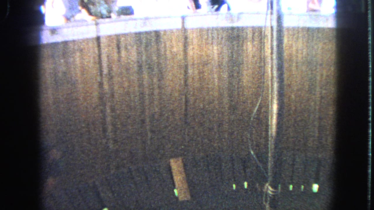 1963 Walworth, Wisconsin 8mm frame showing a dim ride enclosure, central pole, small green lights, and spectators above.