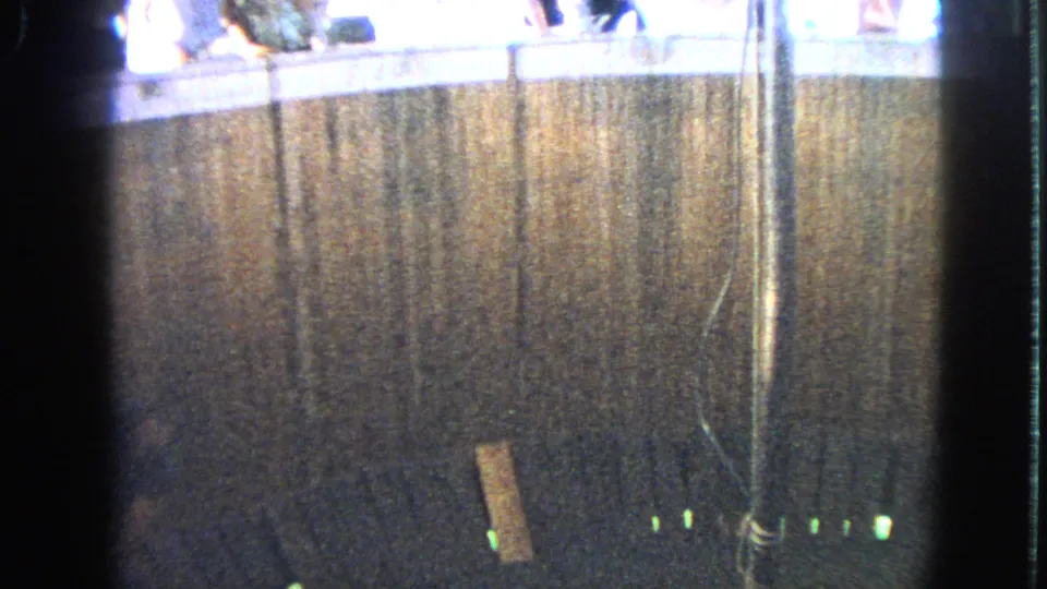 1963 Walworth, Wisconsin 8mm frame showing a dim ride enclosure, central pole, small green lights, and spectators above.