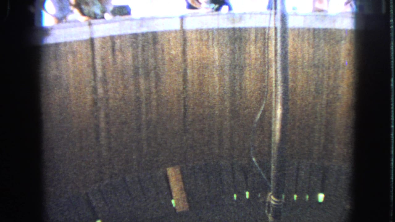1963 Walworth, Wisconsin home-movie frame of a dark amusement-ride space with spectators partly visible above the enclosure.
