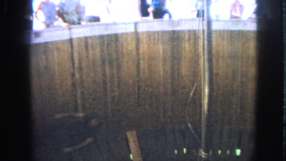 1963 Walworth, Wisconsin 8mm frame showing the ride enclosure from below, with spectators along the bright upper edge.