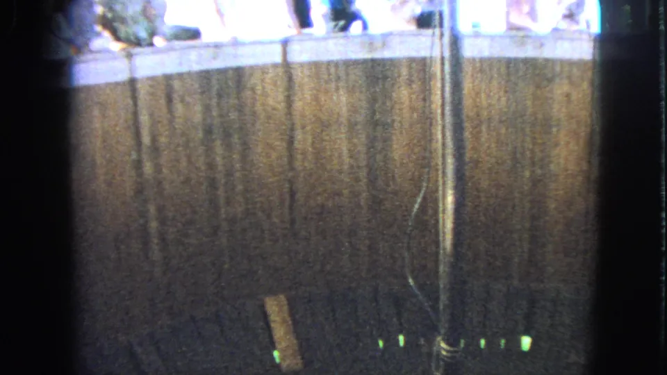 1963 Walworth, Wisconsin frame of a dim amusement-ride enclosure, central pole, green lights, and cropped spectators above.