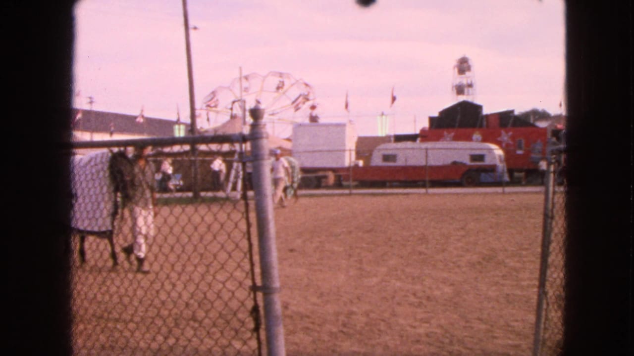 Walworth, Wisconsin 1963 fairground view of a handler with a covered horse near a chain-link fence, with Ferris wheel and trailers behind.