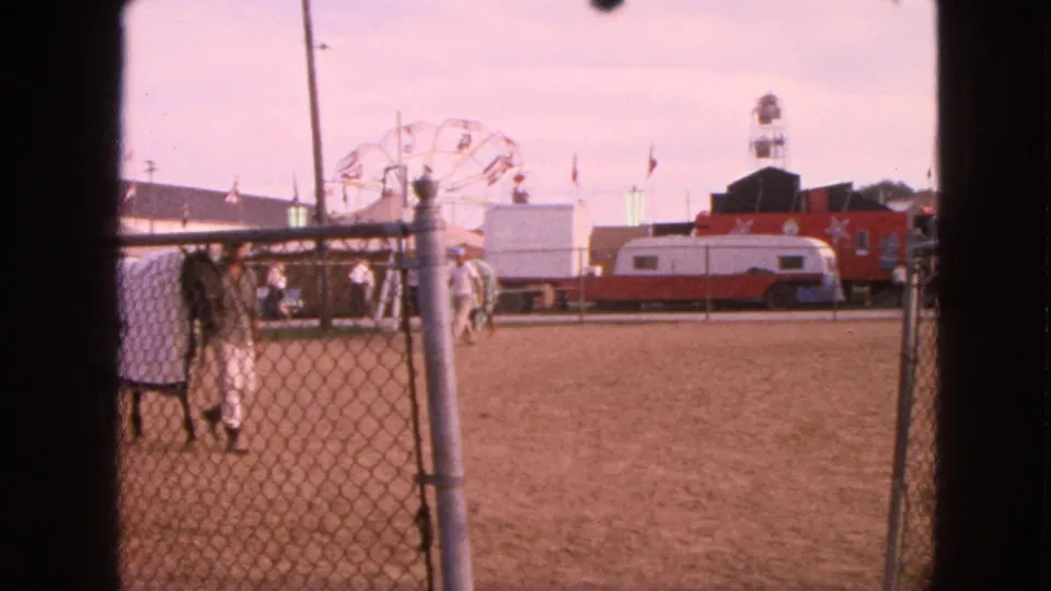 Walworth, Wisconsin 1963 fairground view of a handler with a covered horse near a chain-link fence, with Ferris wheel and trailers behind.