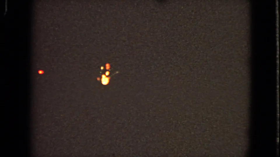 The final frame is mostly dark and underexposed, with only small warm and red lights visible against the film grain.