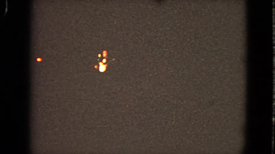 Grainy 1963 home-movie frame from Walworth, Wisconsin showing distant red and orange lights before the stage is visible.