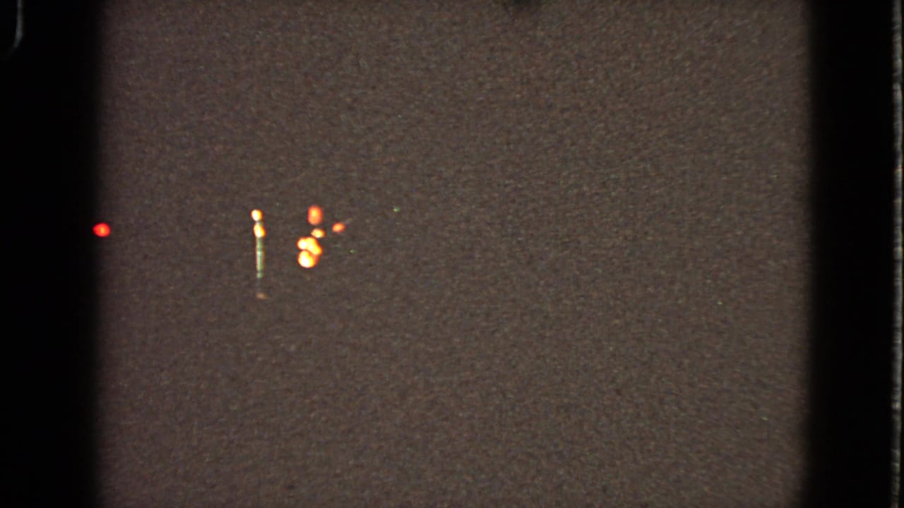Low-light 8mm frame from the Walworth theater clip showing scattered red and amber lights in a dark night setting.