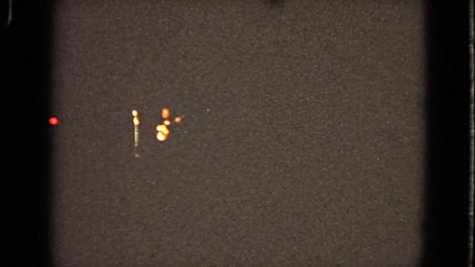 Low-light 8mm frame from the Walworth theater clip showing scattered red and amber lights in a dark night setting.