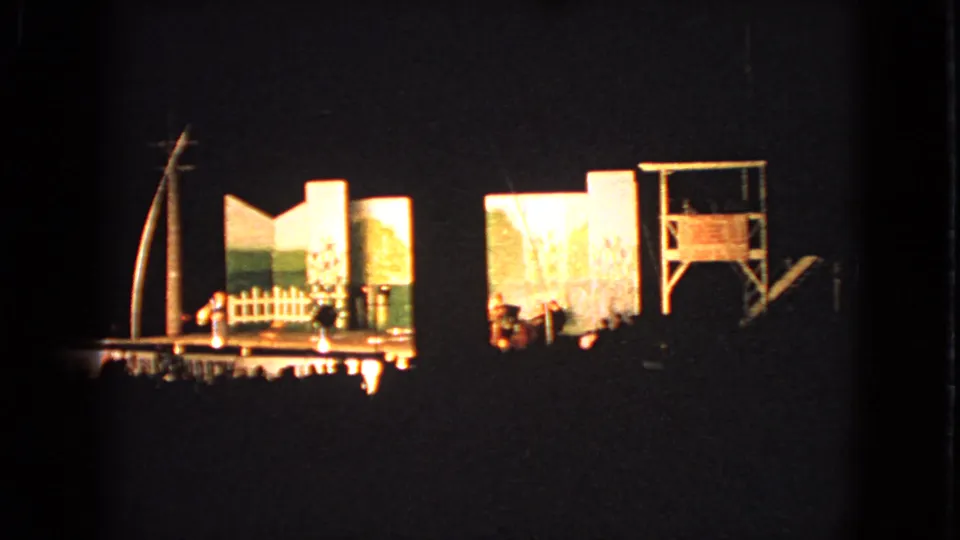 1963 Walworth, Wisconsin home-movie frame showing a night community theater stage with set pieces and audience silhouettes.
