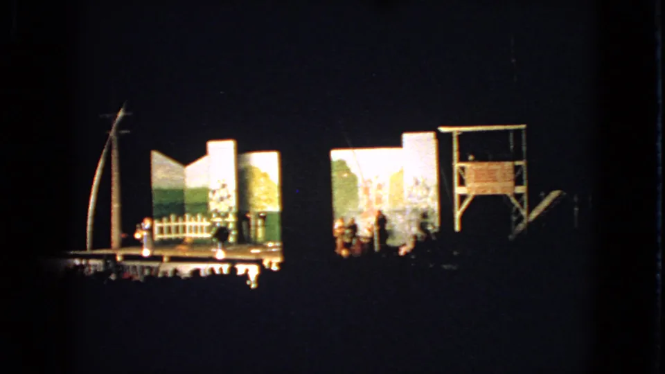 Walworth, Wisconsin 1963 frame showing a dimly filmed community theater stage with actors and audience visible in silhouette.