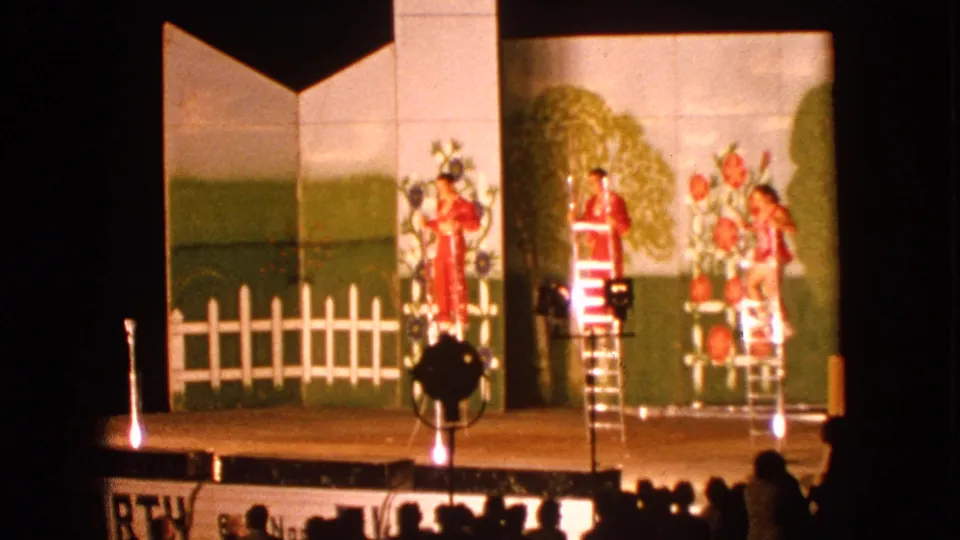 Final 1963 Walworth frame shows multiple performers in red around ladders, with painted flowers and trees behind them and viewers silhouetted below.