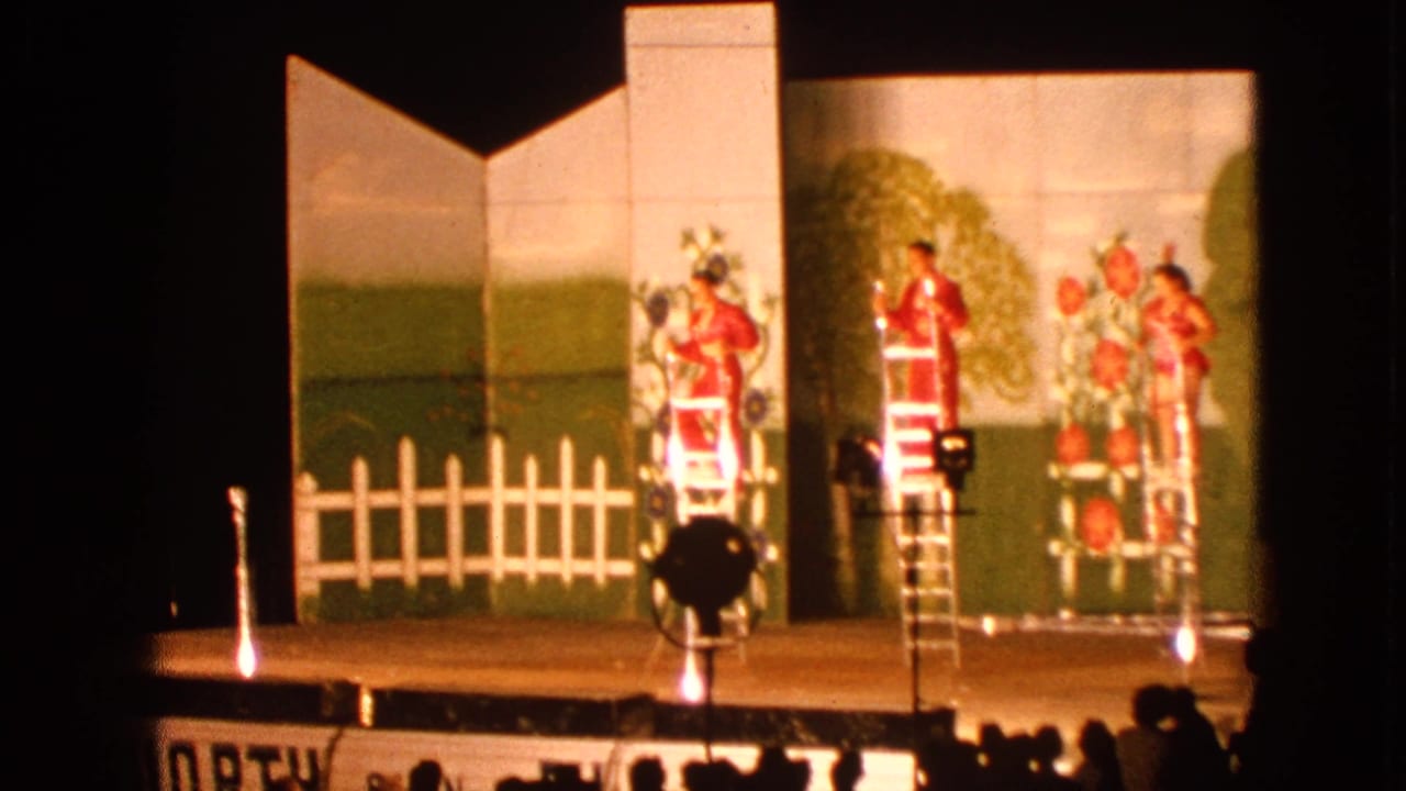 Red-costumed performers stand on ladders on a small stage with a painted outdoor backdrop.