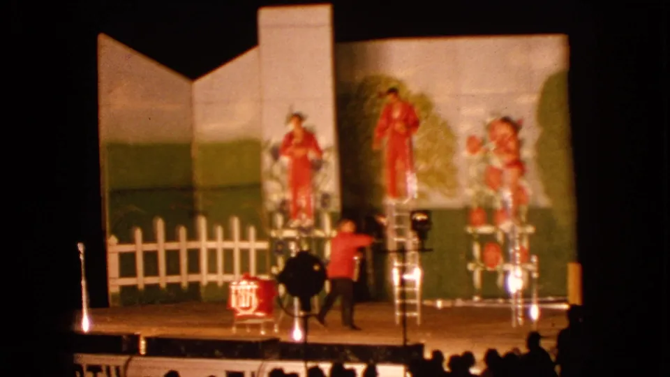 1963 Walworth, Wisconsin home-movie frame showing ladder performers, a stagehand or musician below, and a drum near the front of the stage.