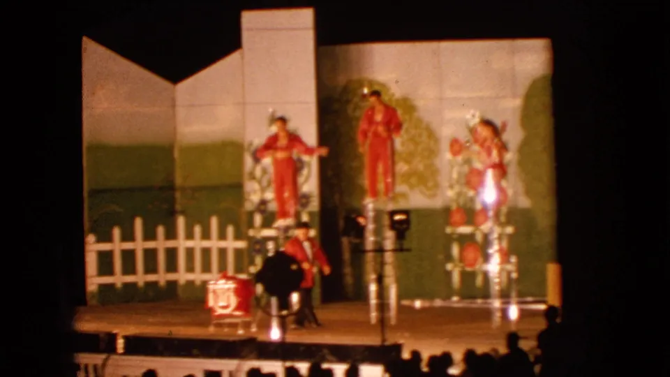 1963 Walworth, Wisconsin frame showing several red-costumed performers on ladders across a community stage with a painted backdrop.