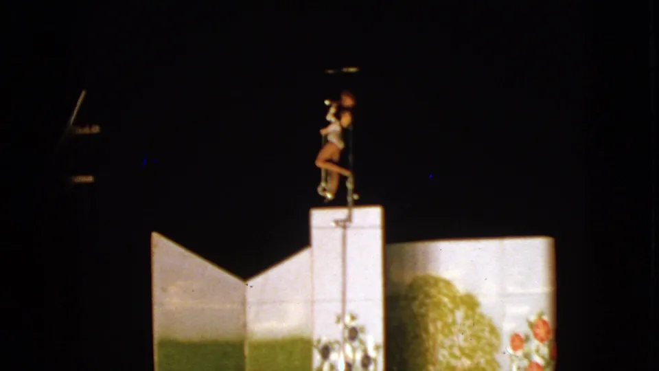 1963 Walworth, Wisconsin frame showing a costumed performer posing with one leg raised on a narrow pole over painted stage panels.