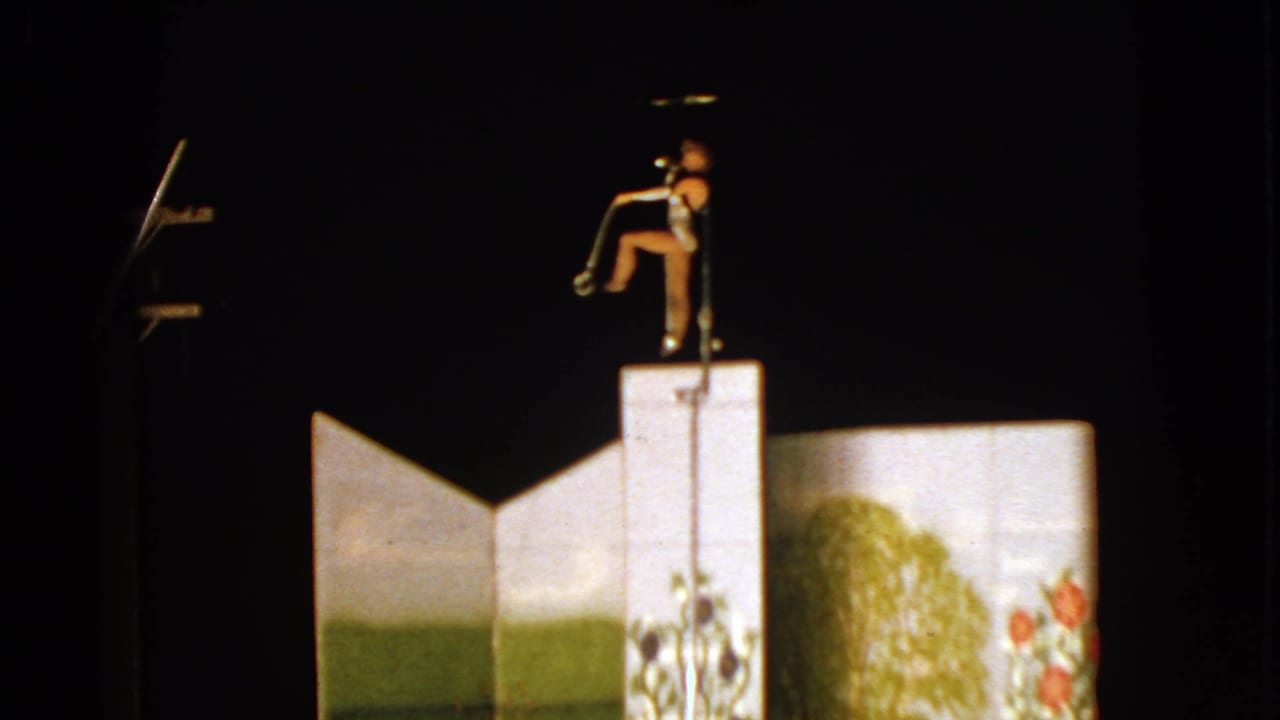 Female trapeze performer above a stage-lit backdrop in 1963 Walworth, Wisconsin home-movie footage.