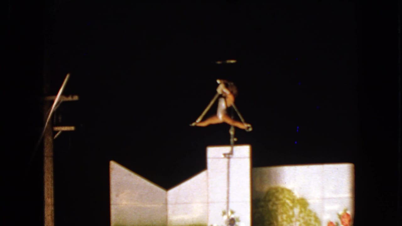Trapeze artist holds a split pose over the illuminated backdrop.
