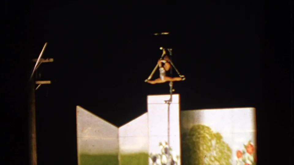 Aerialist suspended in a split pose above a painted backdrop in 1963 Wisconsin 8mm footage.