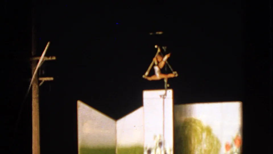Trapeze performer hangs above the backdrop in a nighttime 1963 Walworth home-movie frame.