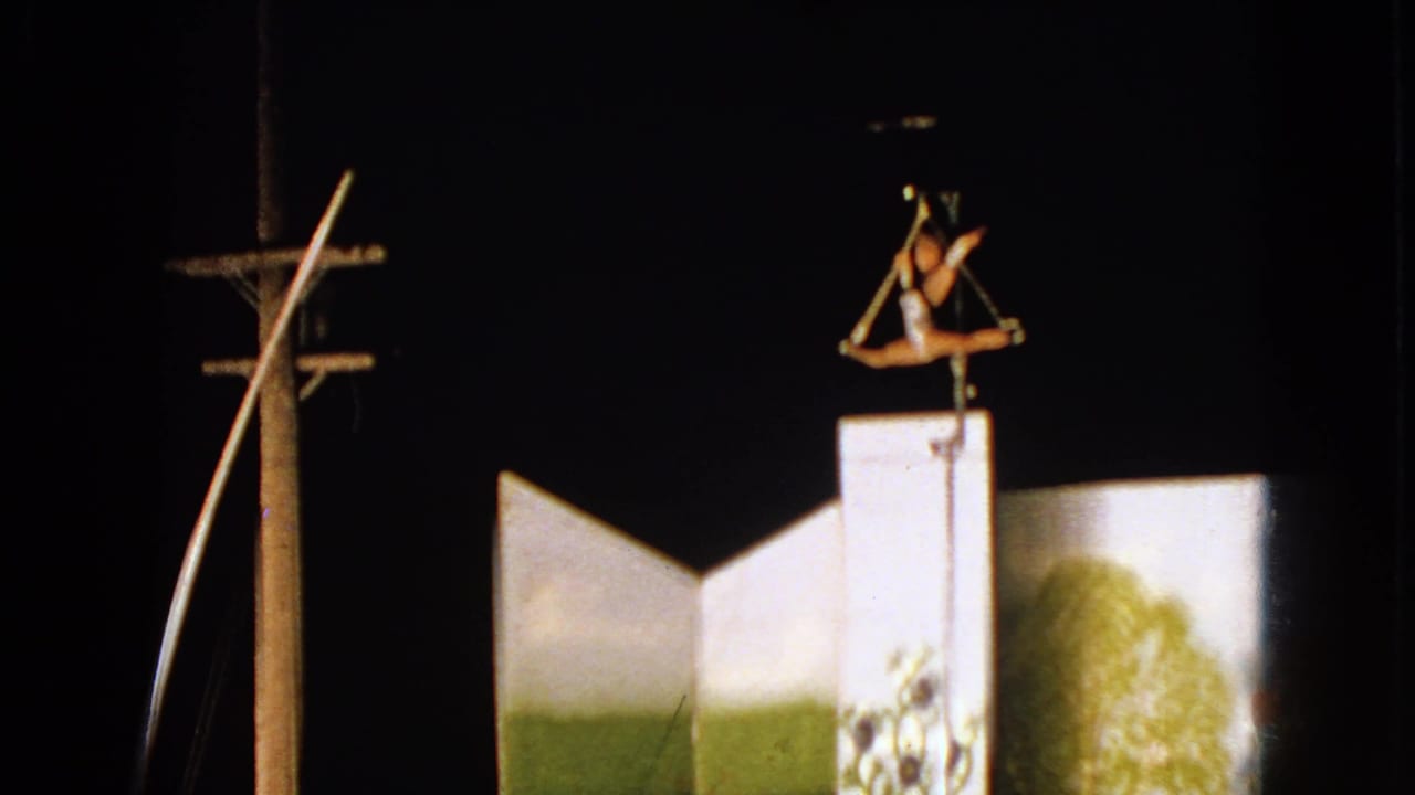 1963 Walworth, Wisconsin frame with a trapeze performer above a tall white circus platform, filmed against a dark night sky.