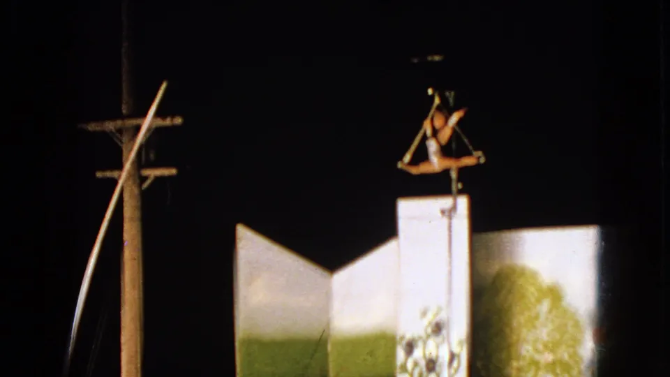 1963 Walworth, Wisconsin frame with a trapeze performer above a tall white circus platform, filmed against a dark night sky.