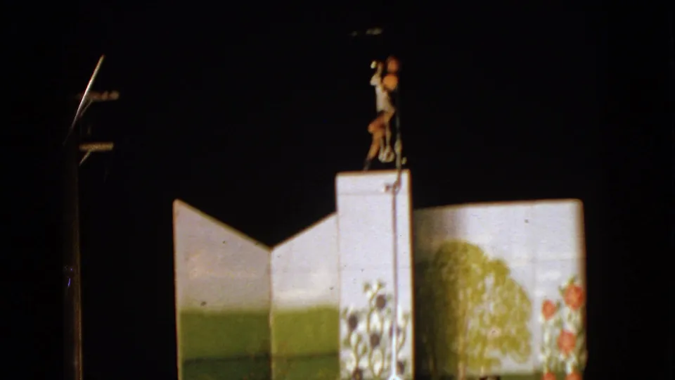 1963 Walworth, Wisconsin frame showing the performer on a raised white platform beside painted set panels under night lighting.