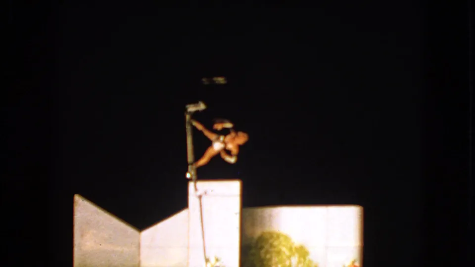 A spotlight catches the acrobat in a compact pole pose during the 1963 Walworth circus performance footage.
