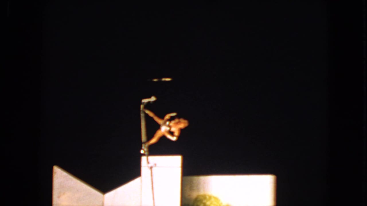 1963 Walworth, Wisconsin 8mm frame showing an acrobat extended sideways on a pole under a spotlight against a dark sky.