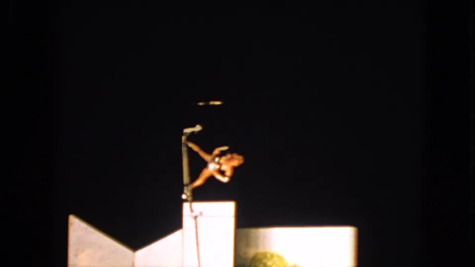 1963 Walworth, Wisconsin 8mm frame showing an acrobat extended sideways on a pole under a spotlight against a dark sky.